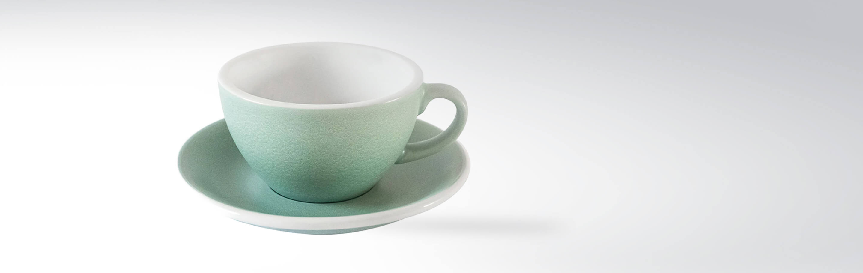 Grüne Keramiktasse mit passender Untertasse auf grauem Hintergrund