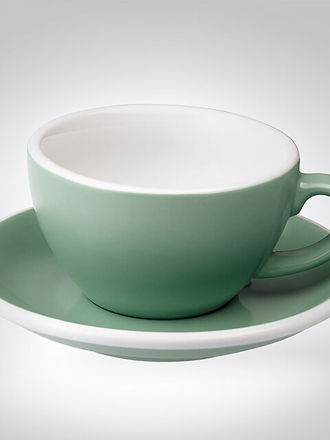 Grüne Porzellantasse mit passender Untertasse auf weißem Hintergrund