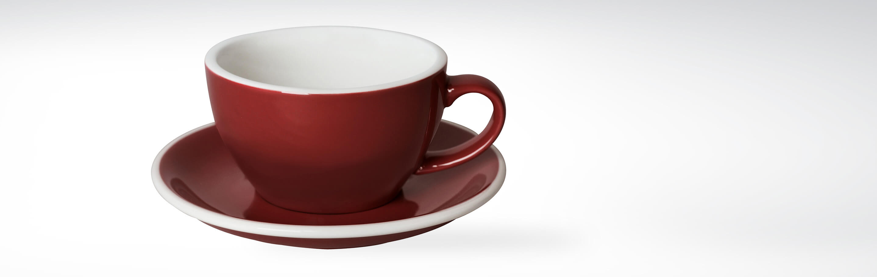 Rote Kaffeetasse mit weißer Innenseite auf passender Untertasse, aus Keramik