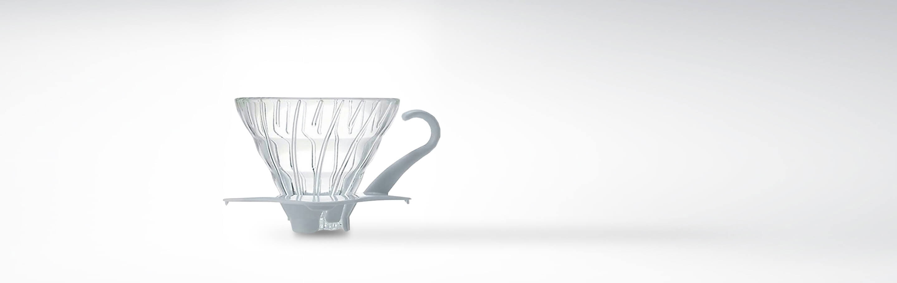 Ein transparenter Kaffeedauerfilter aus Glas mit einem grauen Griff auf weißem Hintergrund