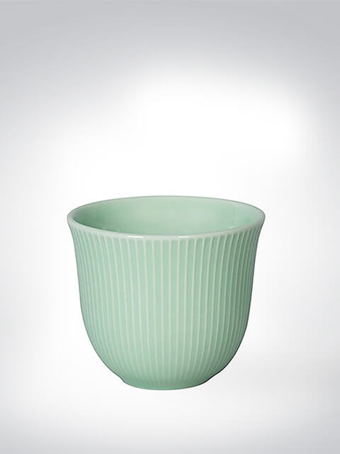Mintgrüner Keramikbecher mit vertikalem Rillenmuster vor grauem Hintergrund