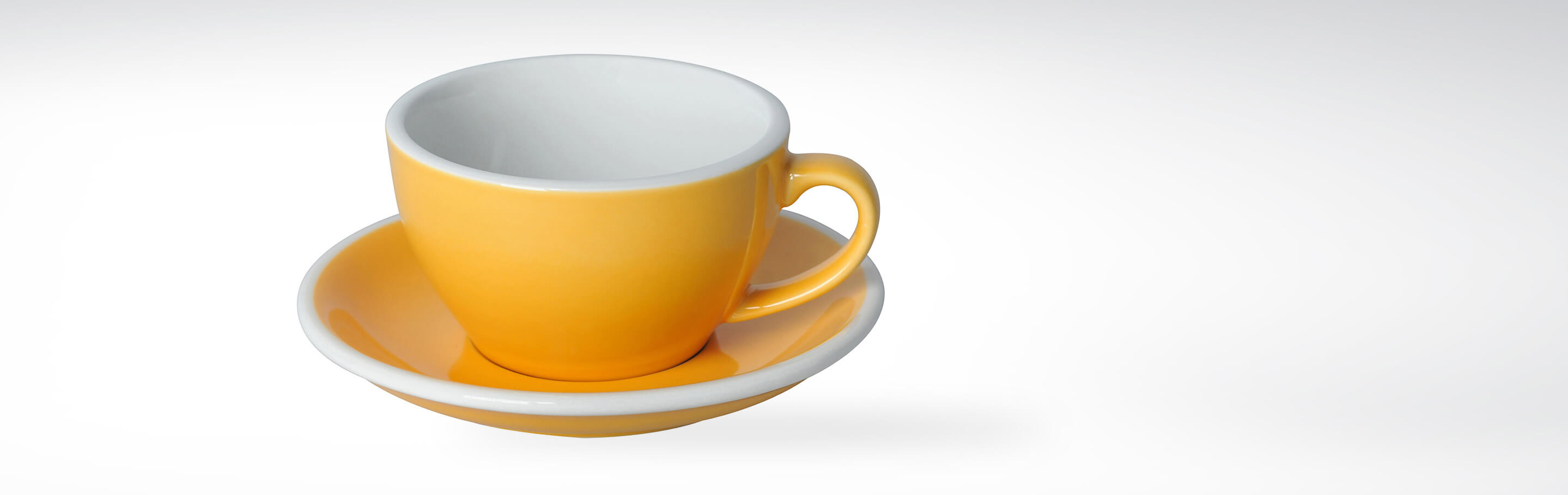 Eine gelbe Kaffeetasse mit passender Untertasse aus Keramik, schlichtes Design auf weißem Hintergrund