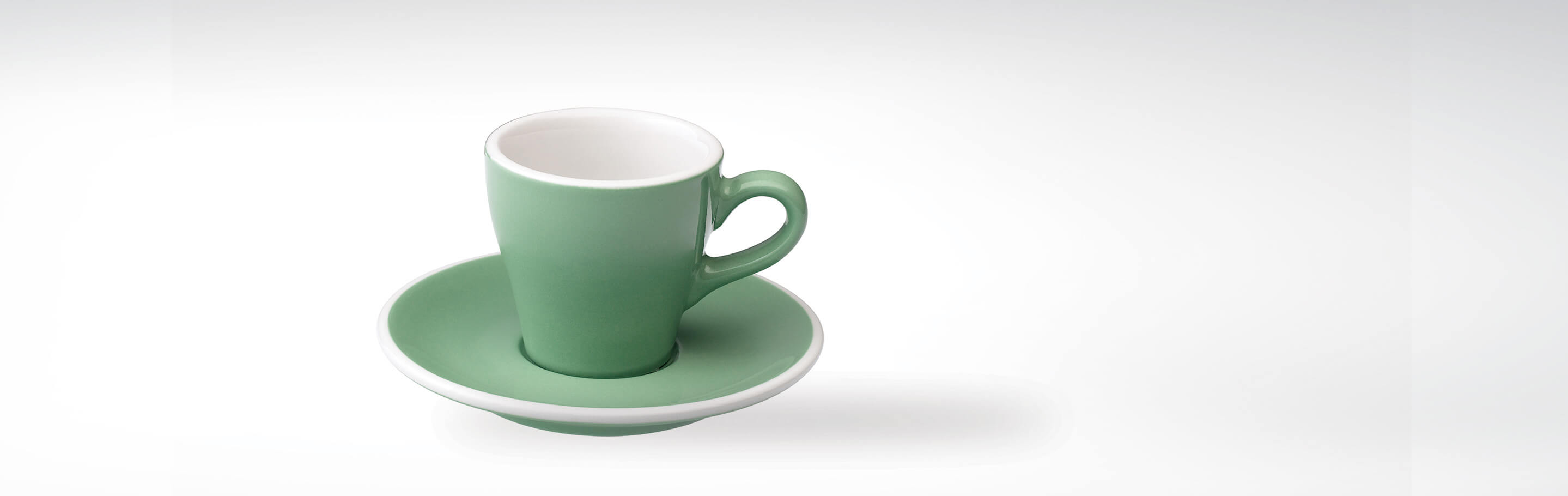 Grün-weiße Kaffeetasse auf weißem Hintergrund, dekorativ arrangiert mit passender Untertasse