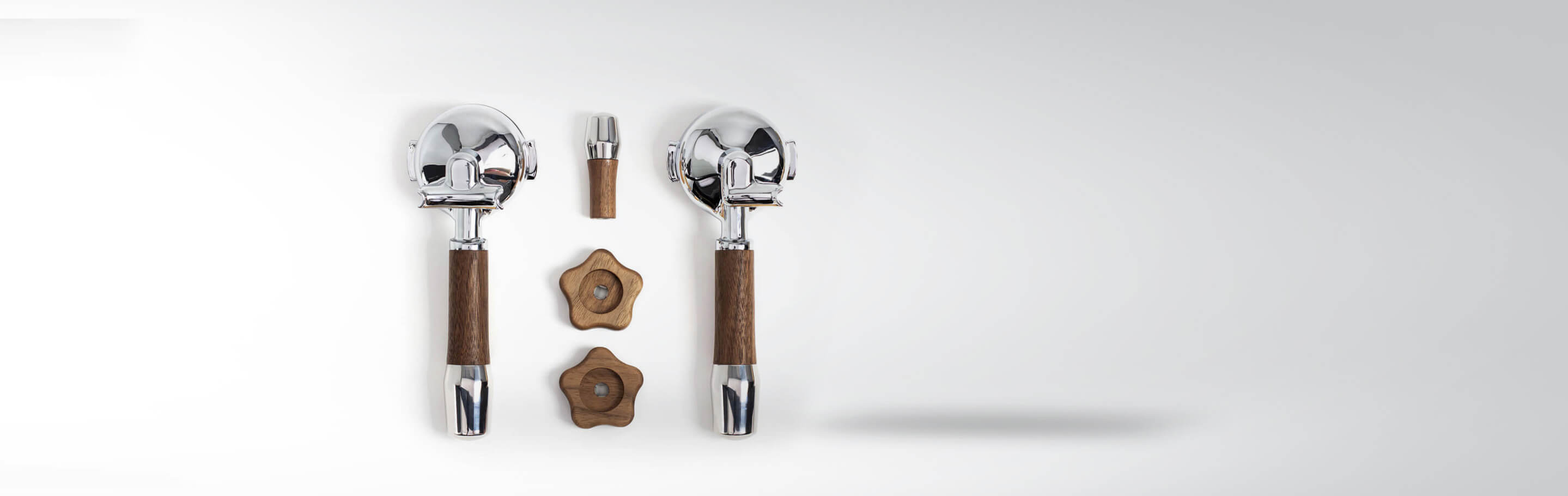 Siebträgereinheit und Zubehör, bestehend aus zwei Siebträgern mit Holzgriff, einem zusätzlichen Griffaufsatz und zwei Holzbasis-Elementen, auf weißem Hintergrund dargestellt.