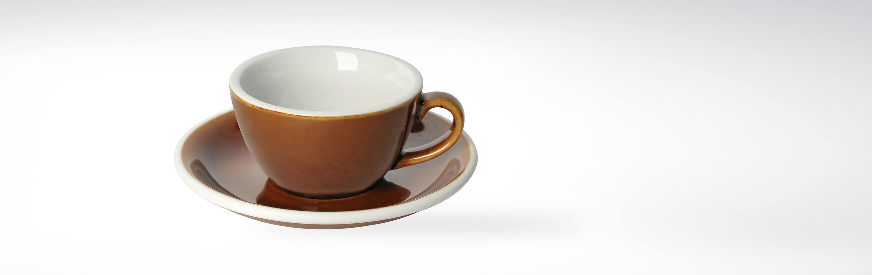 Nahaufnahme einer braunen Espressotasse aus Keramik mit passender Untertasse auf weißem Hintergrund