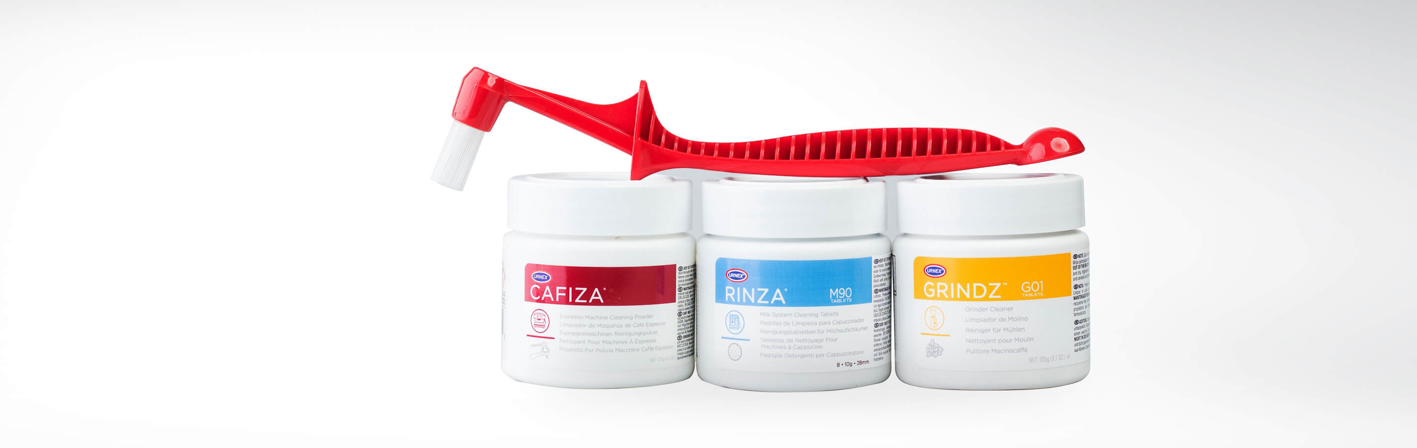 Drei Dosen zur Reinigung von Espressomaschinen und Mühlen mit einer roten Bürste auf weißem Hintergrund
