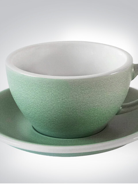 Nahaufnahme einer grünen Keramiktasse auf passender Untertasse, minimalistisches Design auf hellem Hintergrund