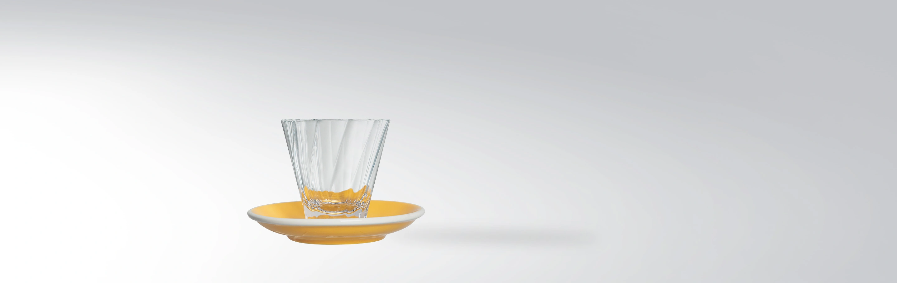 Ein elegantes Trinkglas auf einem gelben Keramikunterteller