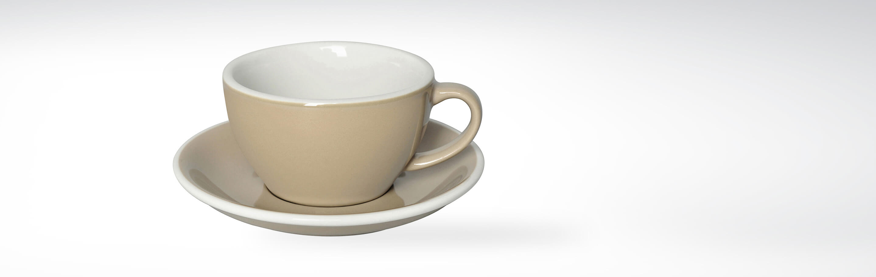 Beige Keramiktasse mit passendem Unterteller auf weißem Hintergrund