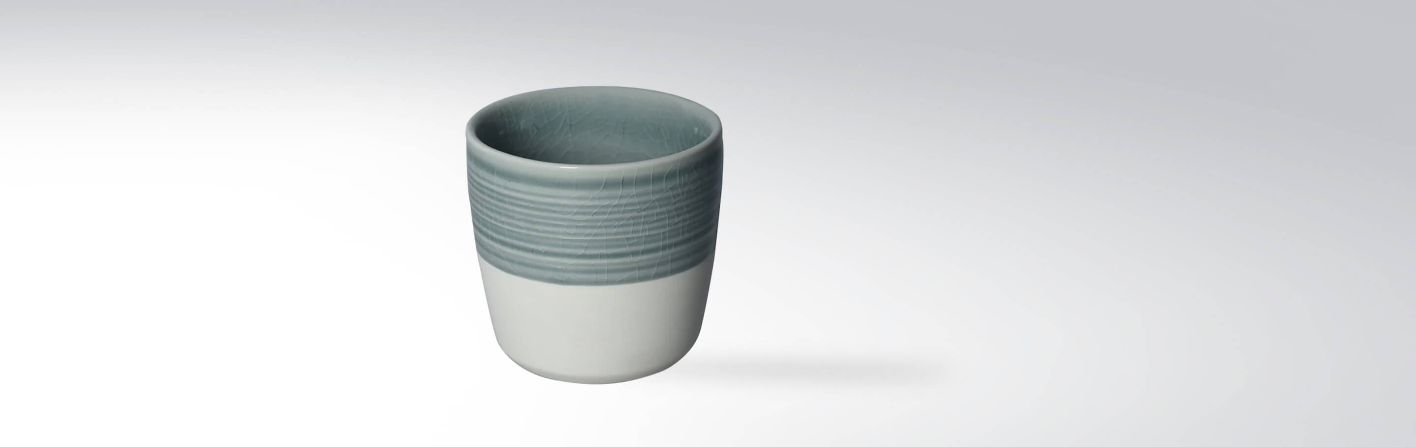 Keramikbecher mit grauer, strukturierter Oberfläche und weißem Boden auf weißem Hintergrund