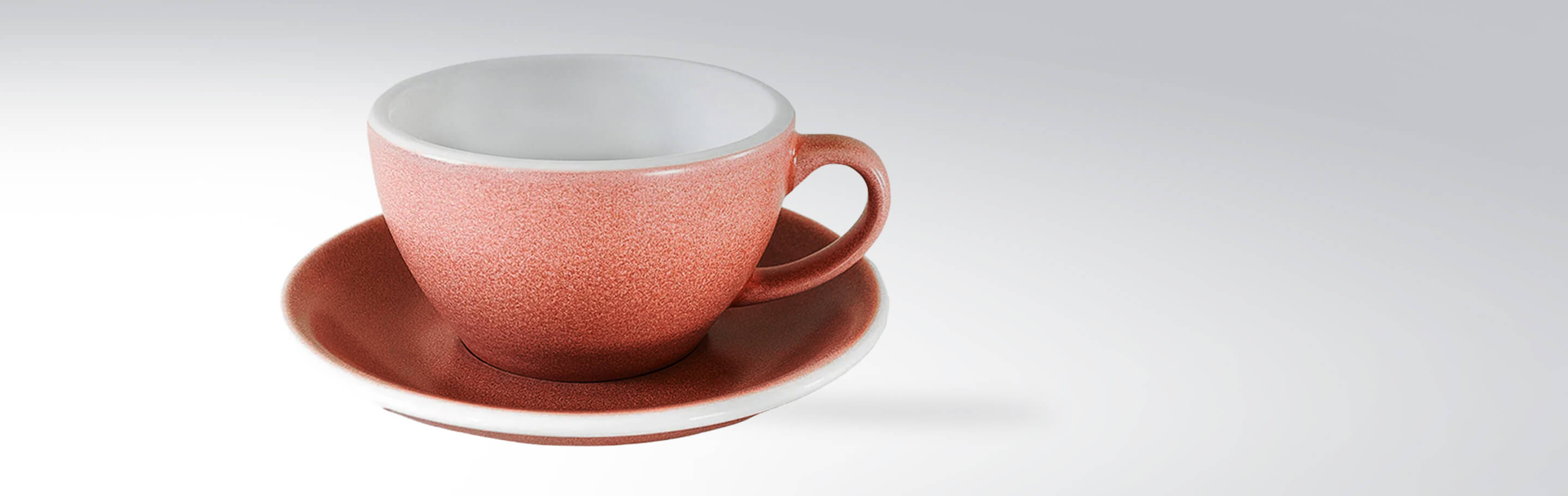 Nahaufnahme einer Keramiktasse mit passender Untertasse in warmem Rotton.