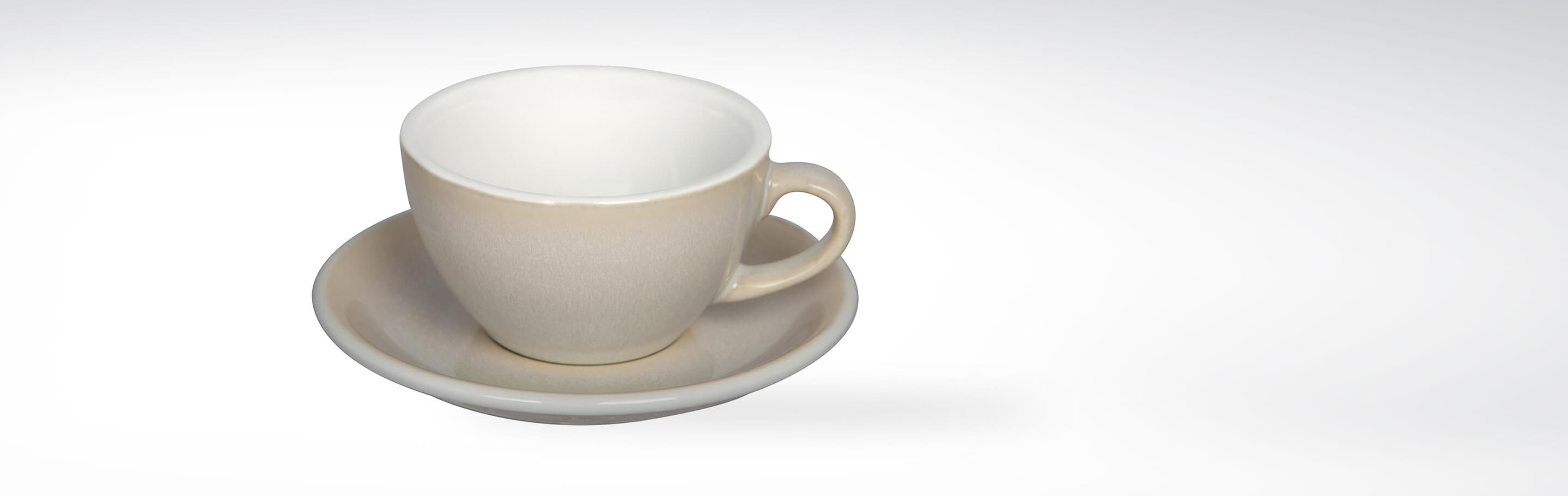 Kaffeetasse mit Untertasse aus hellbeiger Keramik vor weißem Hintergrund