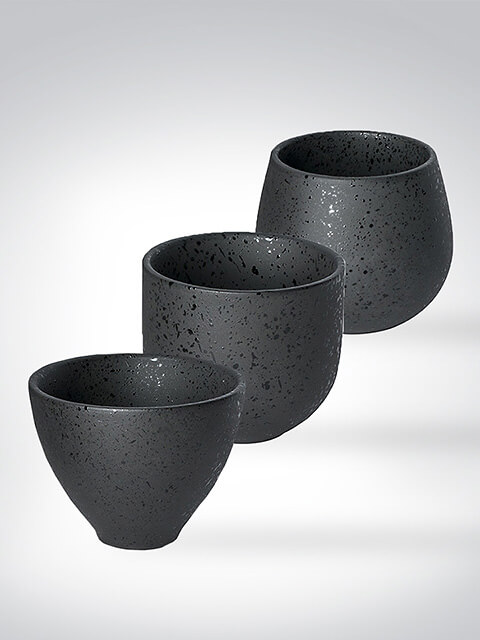 Drei schwarze Keramikbecher in verschiedenen Formen, vor hellem Hintergrund arrangiert