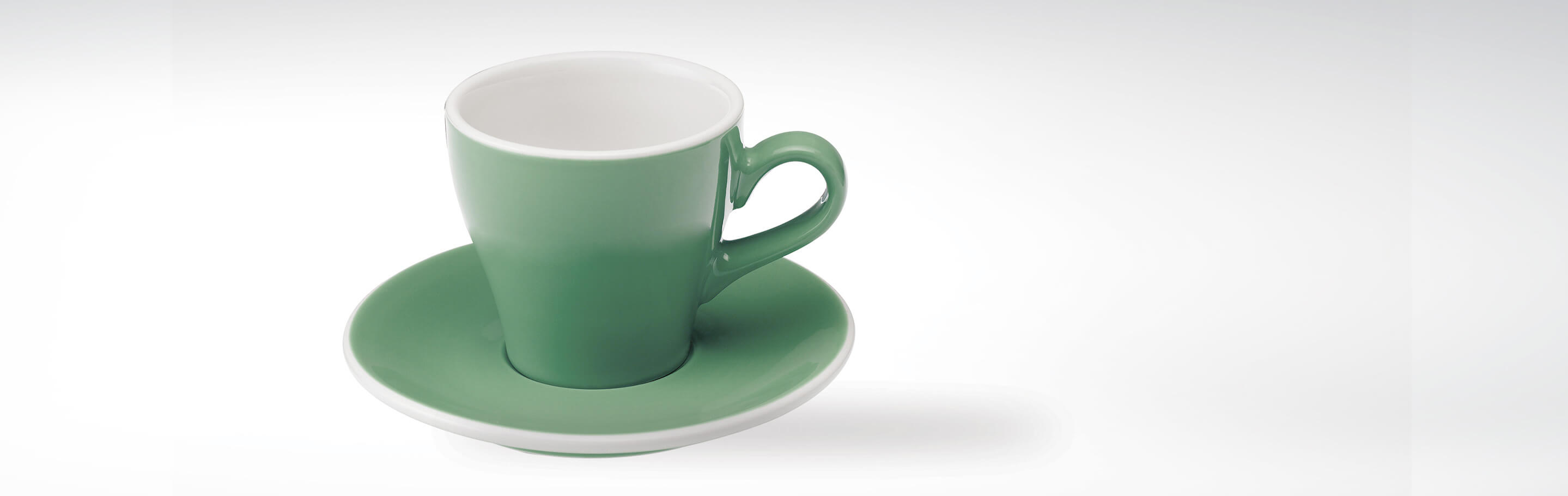 Grüne Keramiktasse mit passender Untertasse auf weißem Hintergrund
