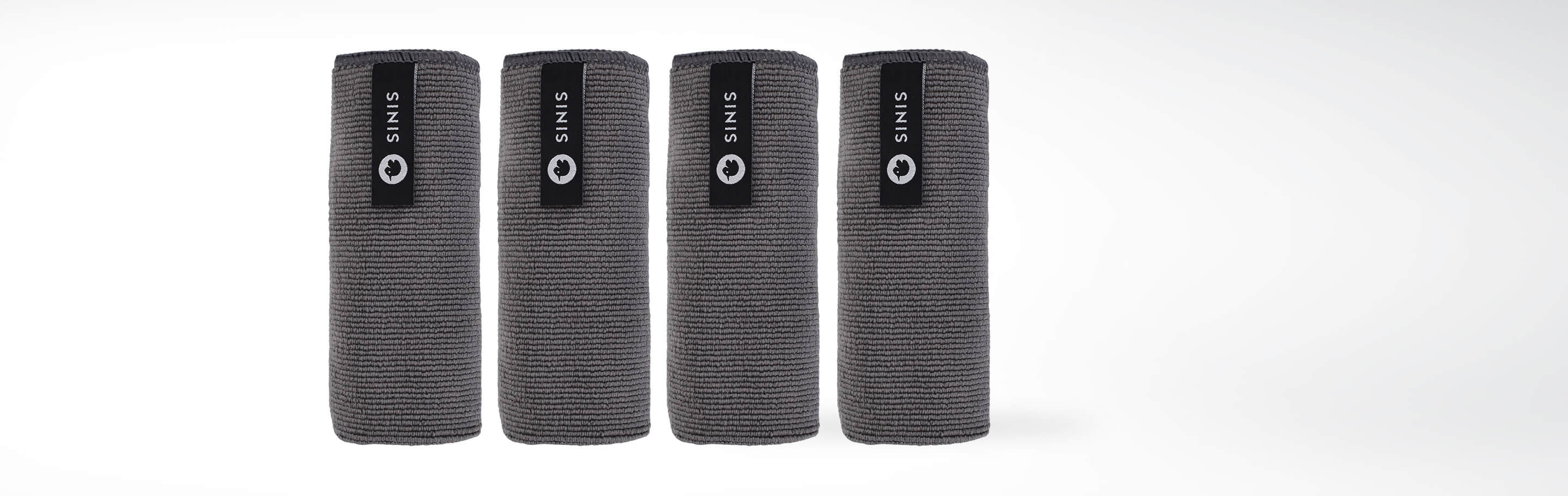 Vier aufgerollte graue Mikrofaser-Handtücher mit schwarzem Sinis-Label nebeneinander