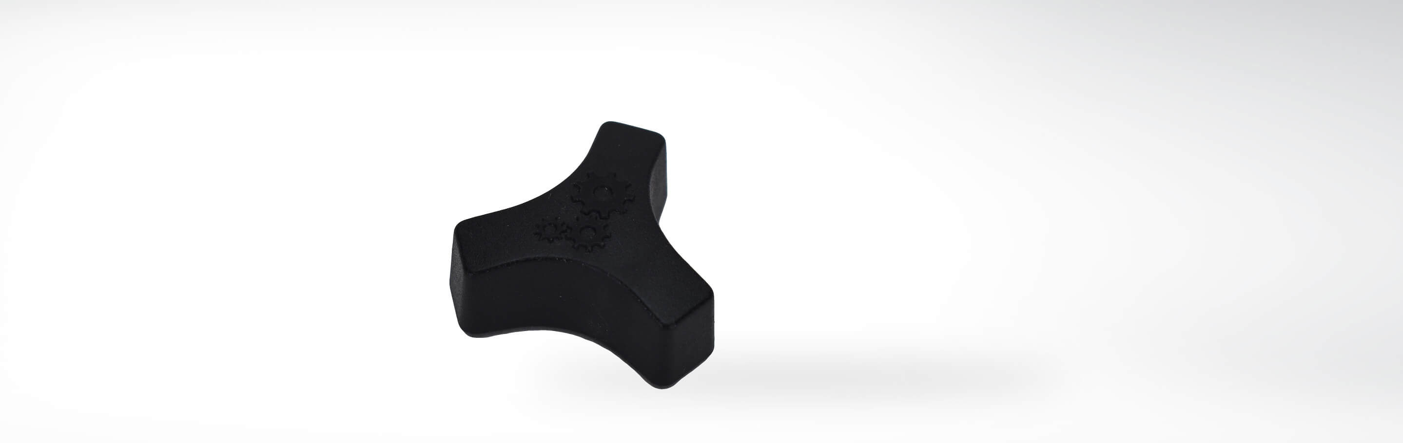 Schwarzes dreieckiges Kunststoffteil mit Zahnradsymbolen, vor weißem Hintergrund