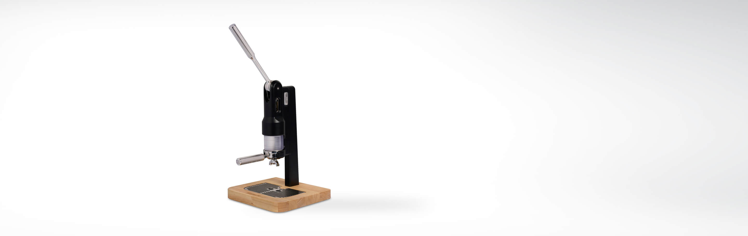 Nahaufnahme einer manuellen Espressomaschine mit langem Hebel, kompakter Bauweise und Holzsockel auf weißem Hintergrund
