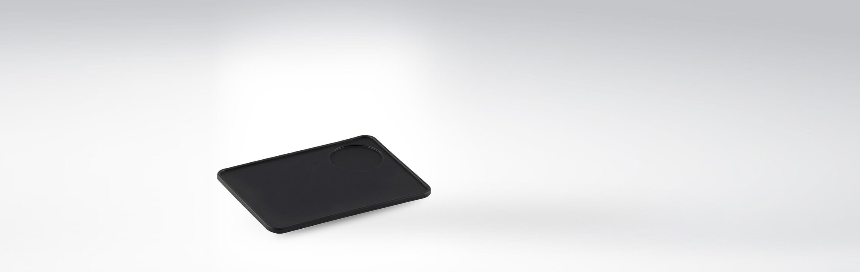 Schwarze Silikonmatte mit integriertem Tassenhalter auf weißem Hintergrund