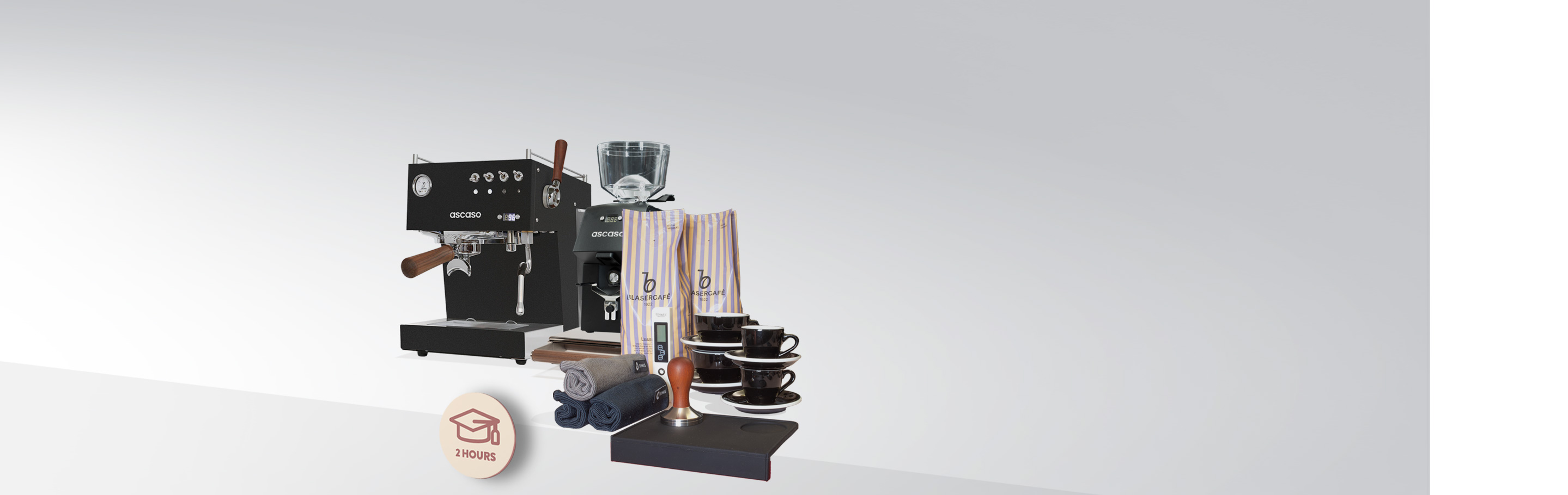 Espressomaschine Ascaso mit Kaffeemühle, zwei Kaffeebohnensäcken, Tamper, Tassen und Handtücher auf einem Tisch angeordnet.