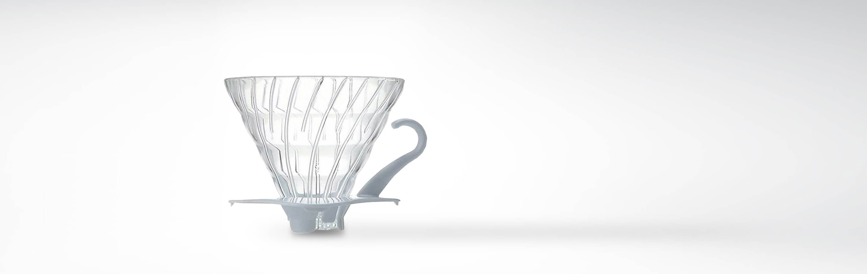 Ein transparenter Kaffeefilteraufsatz aus Plastik mit dekorativem Muster und Griff, fotografiert vor einem weißen Hintergrund.