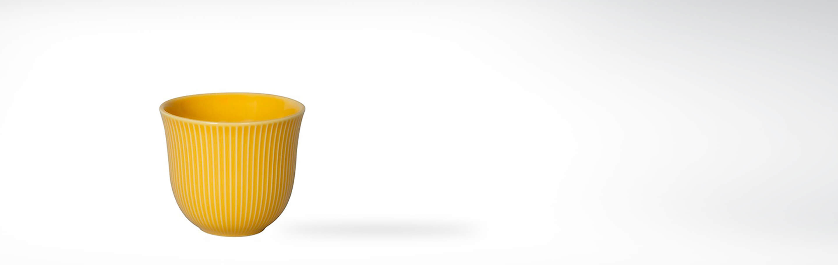Gelber Keramikbecher mit Rillenmuster auf weißem Hintergrund
